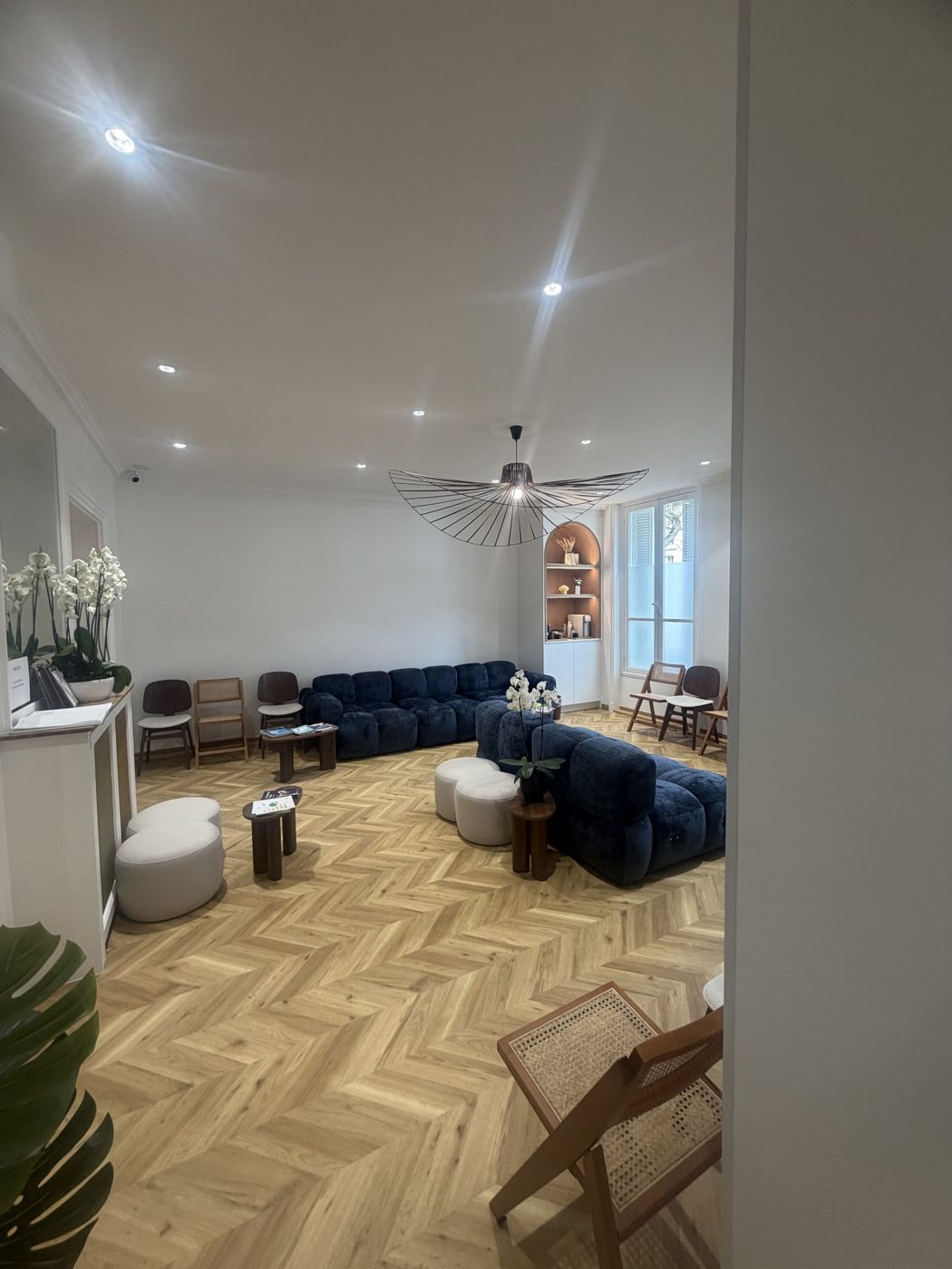 Salle d'attente aménagée avec grand canapé bleu, lustre et parquet à chevrons