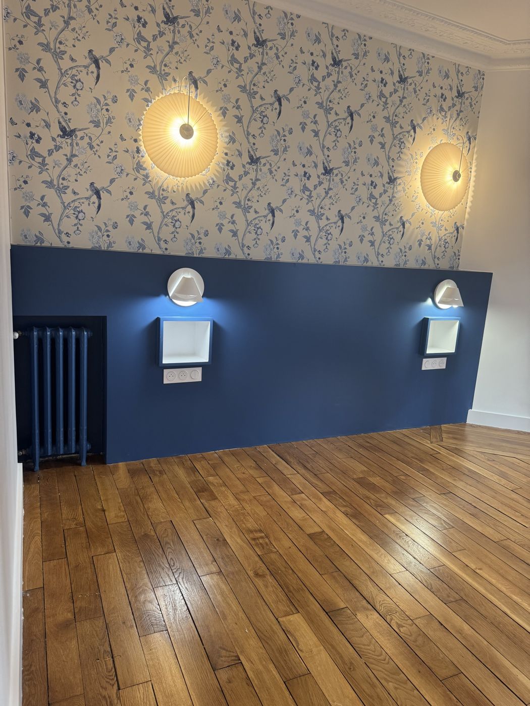 Chambre avec papier peint à oiseaux bleus, tête de lit peinte en bleu et appliques