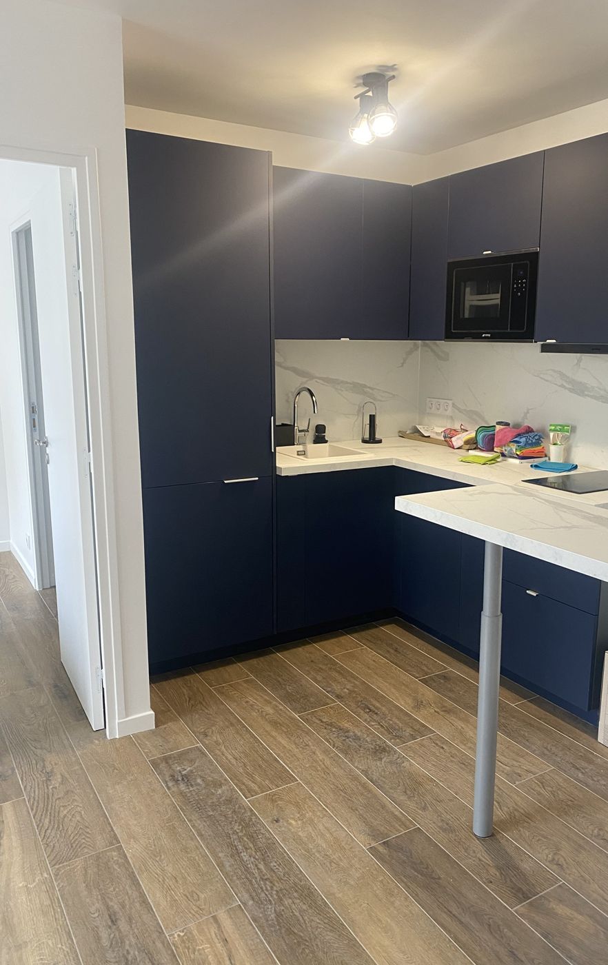 Cuisine en L bleu nuit avec crédence effet marbre et bar