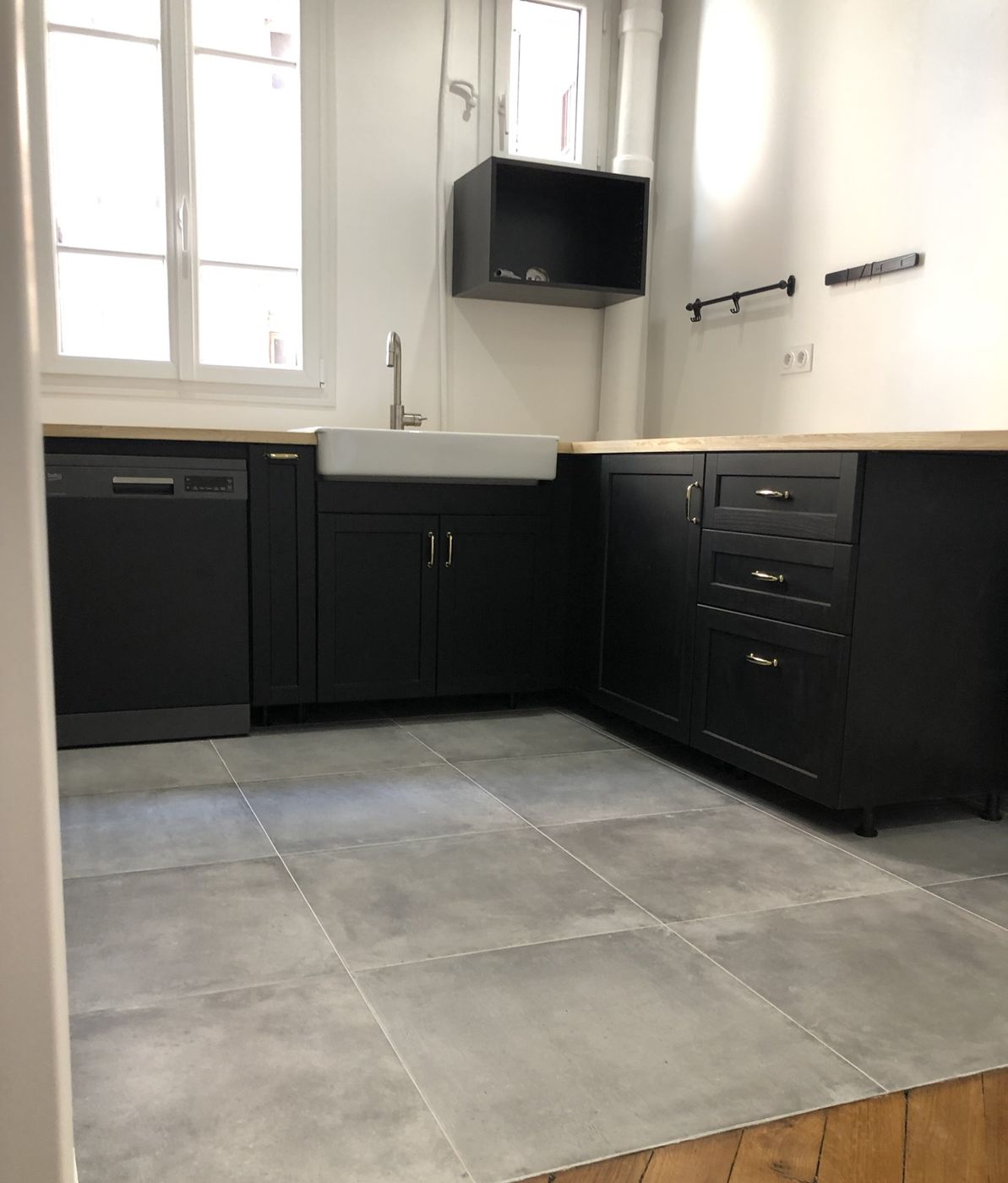 Cuisine noire avec plan de travail en bois, évier en grès blanc et carrelage gris