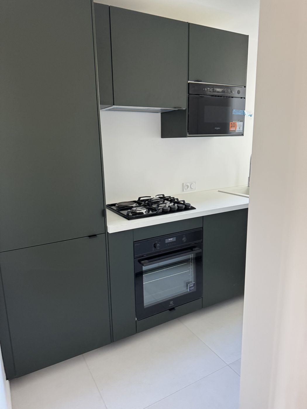 Cuisine vert sapin avec four noir, plaque de cuisson et plan de travail blanc