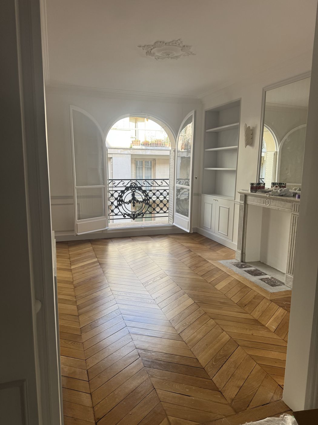 Salon lumineux avec fenêtre en arc, bibliothèque encastrée, cheminée en marbre et parquet à chevrons