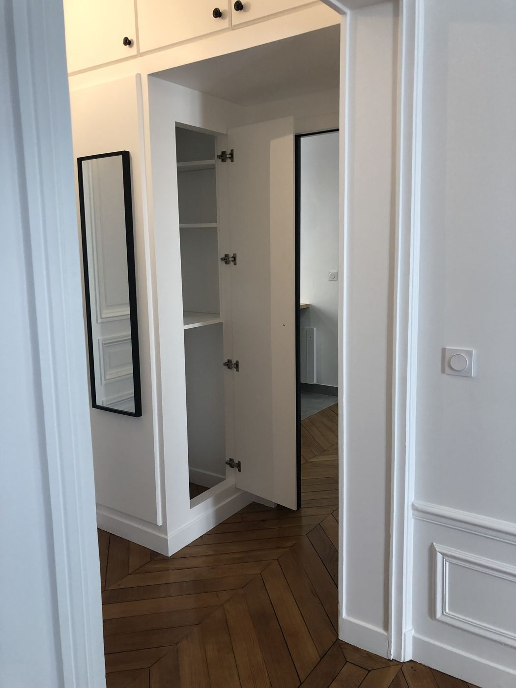 Placard sur mesure et miroir dans un couloir à parquet à chevrons