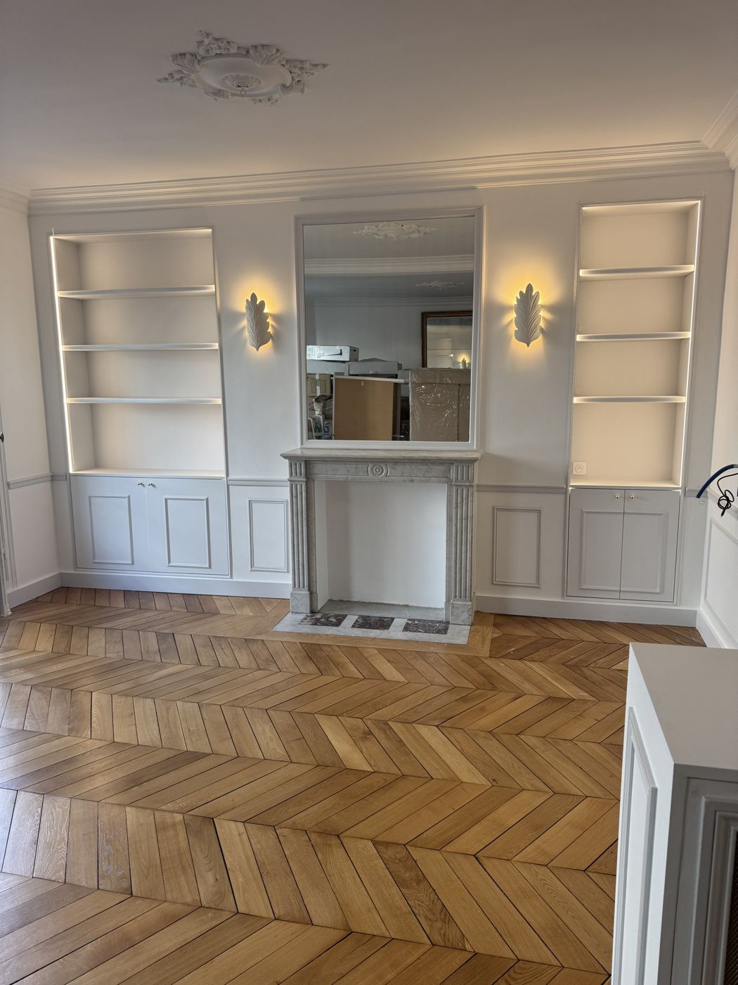 Salon avec bibliothèques encastrées éclairées, cheminée en marbre et parquet à chevrons