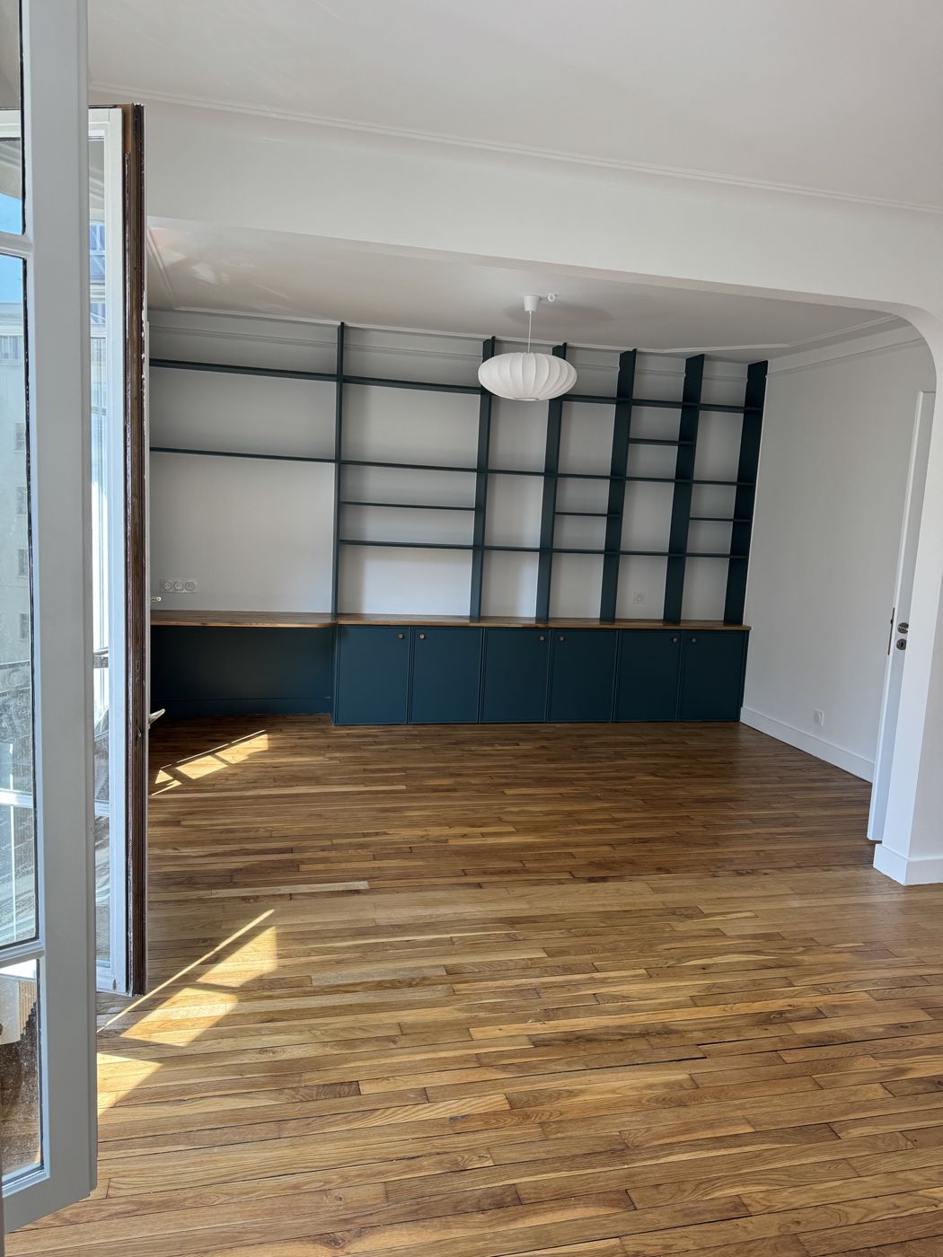 Salon avec grande bibliothèque bleu canard sur mesure, meubles bas et parquet ancien