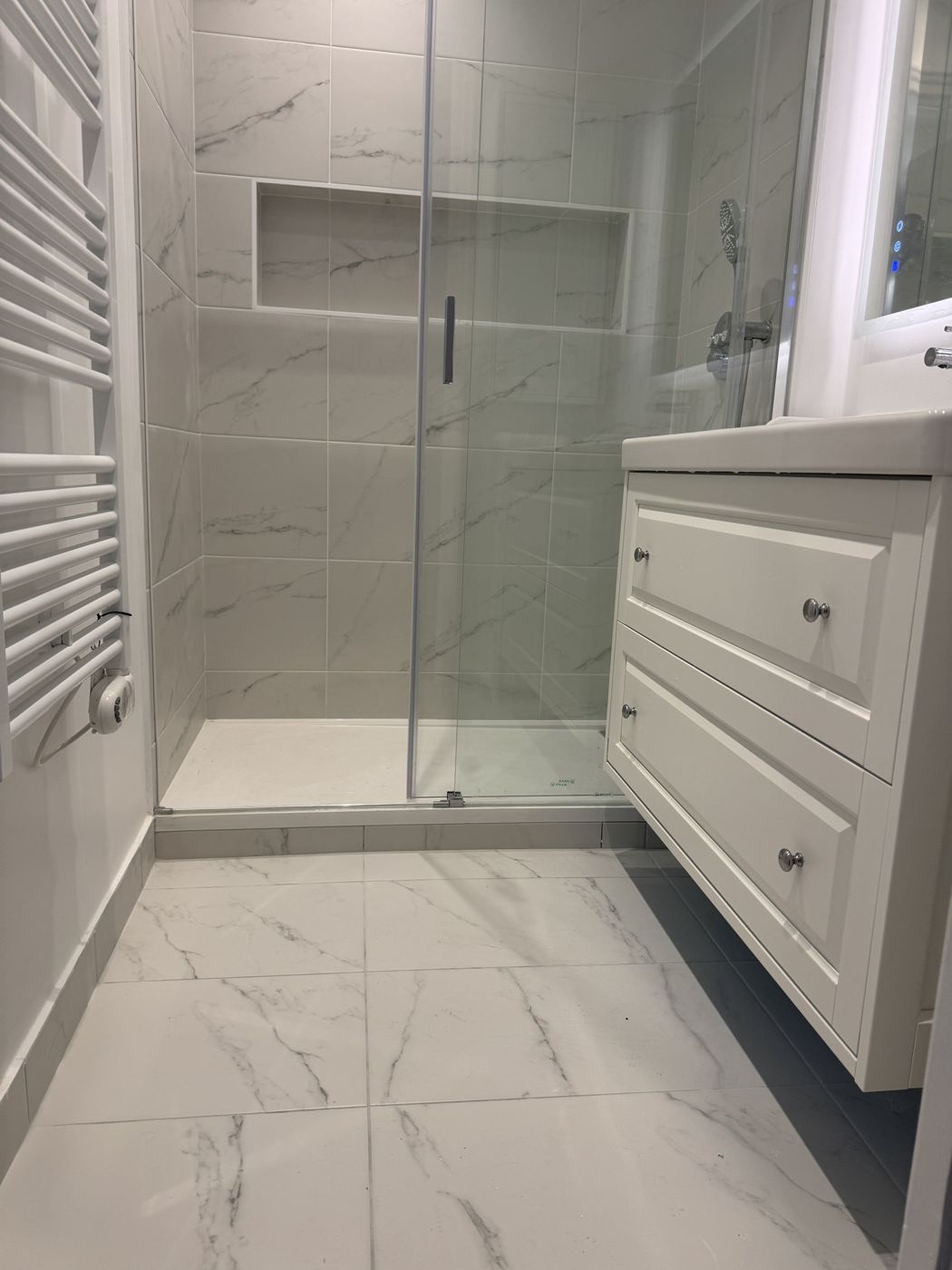 Salle de bain avec douche en carrelage effet marbre et meuble vasque blanc