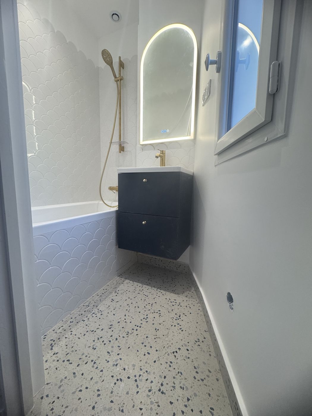 Salle de bain avec carrelage en écailles blanches, miroir arqué éclairé et meuble bleu marine
