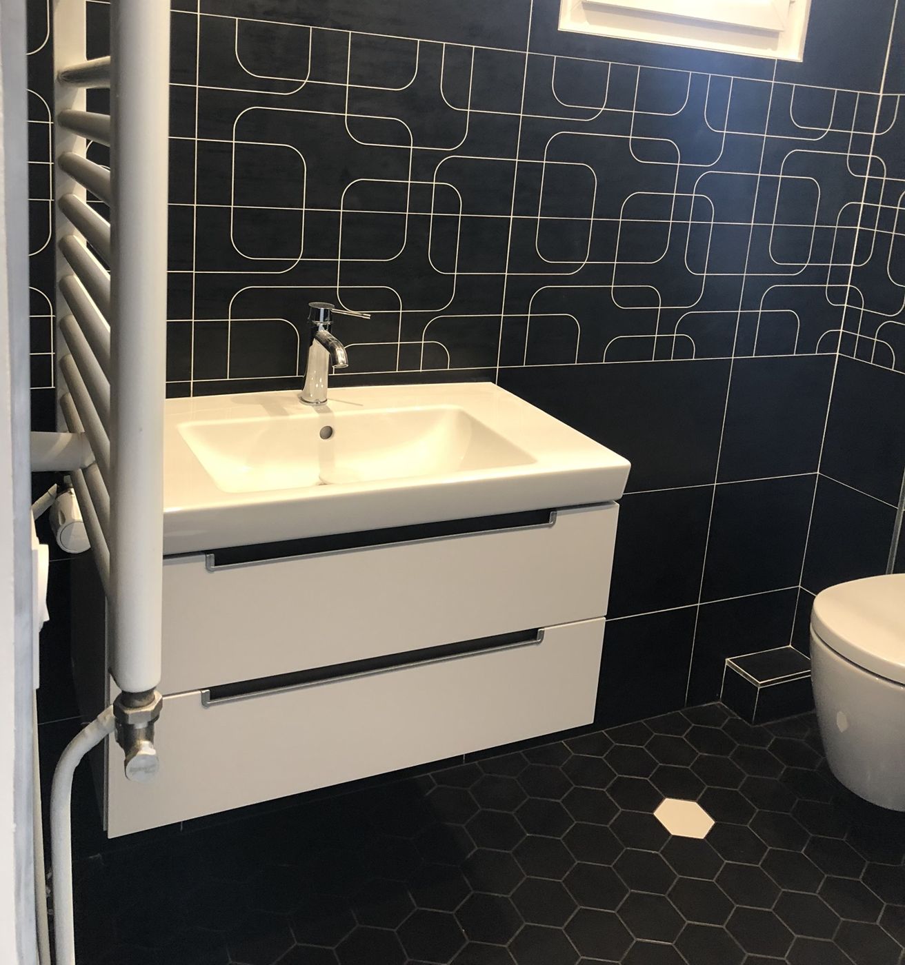 Vasque suspendue blanche sur carrelage noir à motifs