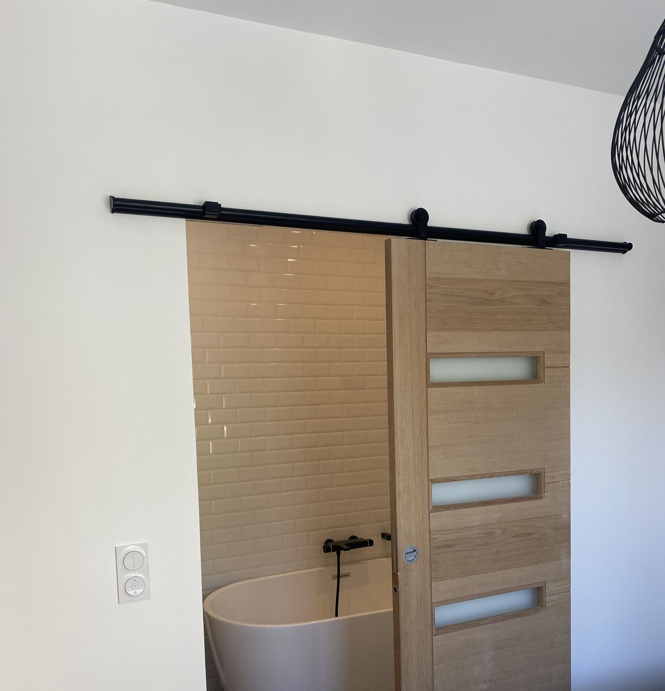 Porte coulissante en chêne sur rail noir ouvrant sur une salle de bain avec baignoire